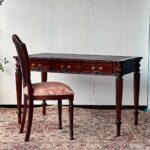 Antique dark wood desk with leather top and matching patterned chair on rug.