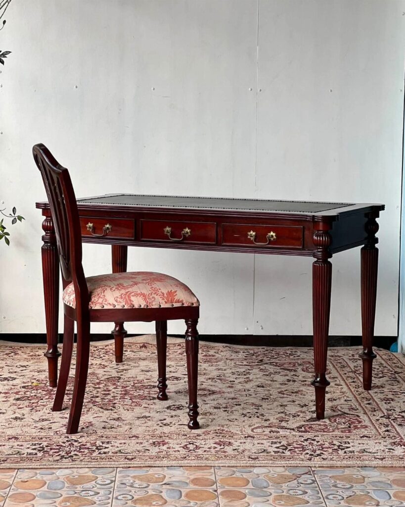 Antique dark wood desk with leather top and matching patterned chair on rug.
