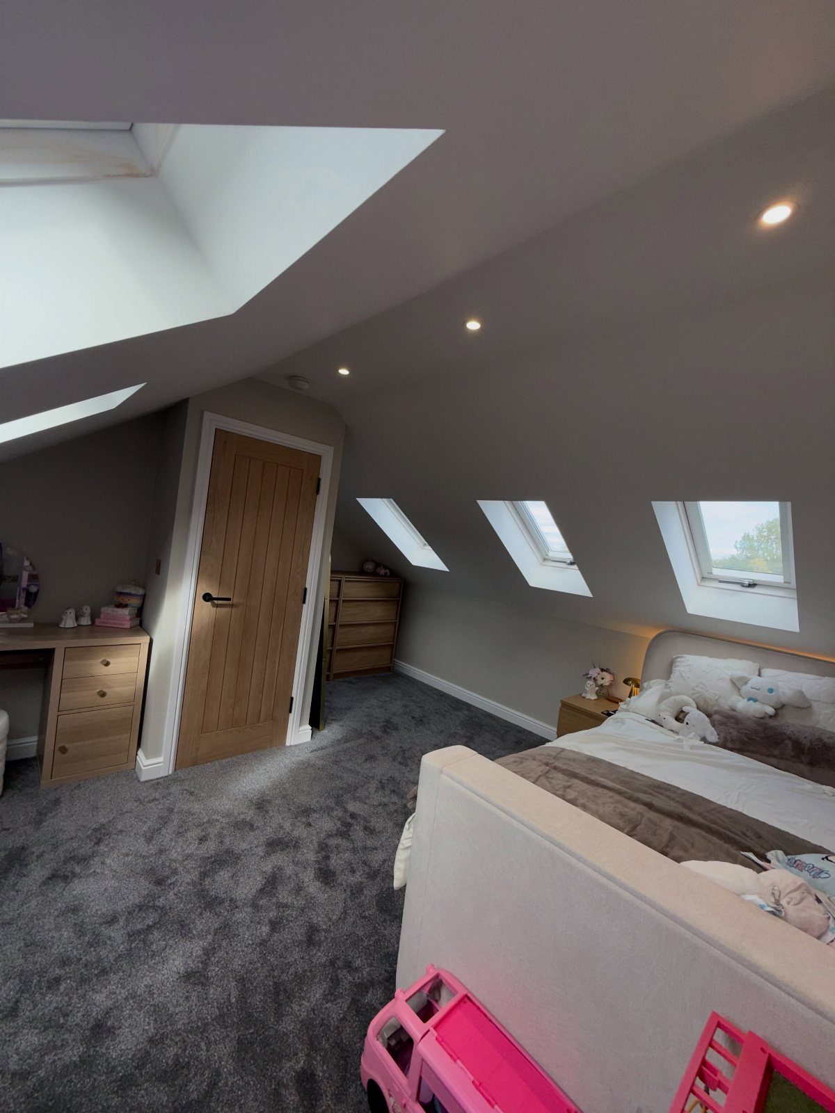 Attic bedroom with sloped ceilings, skylights, grey carpet, and wooden furniture.