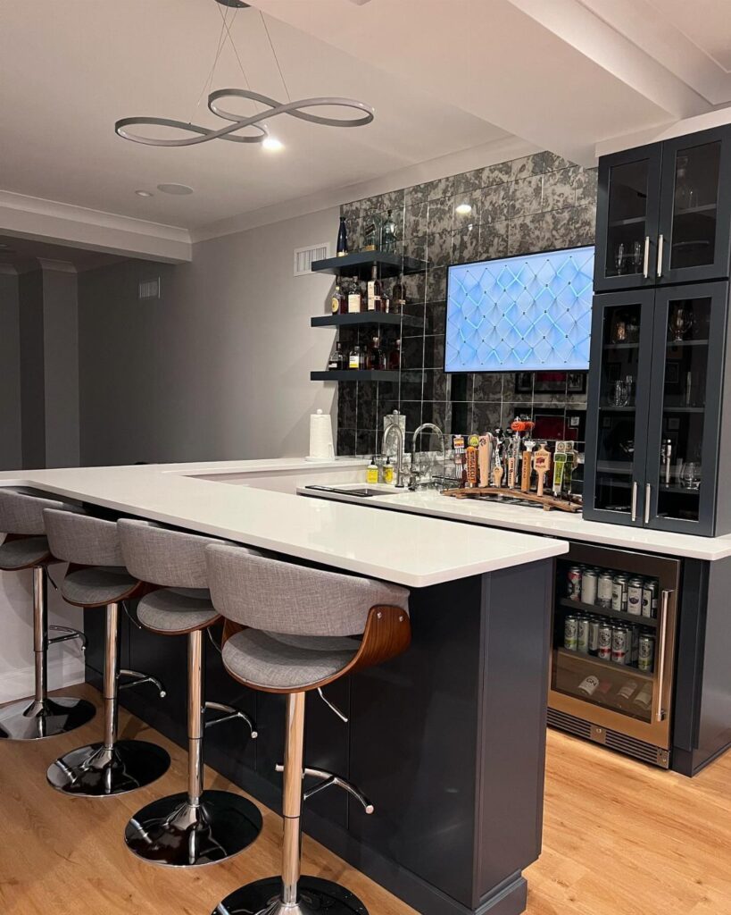 Modern home bar with white countertop, grey stools, and liquor bottle shelving.