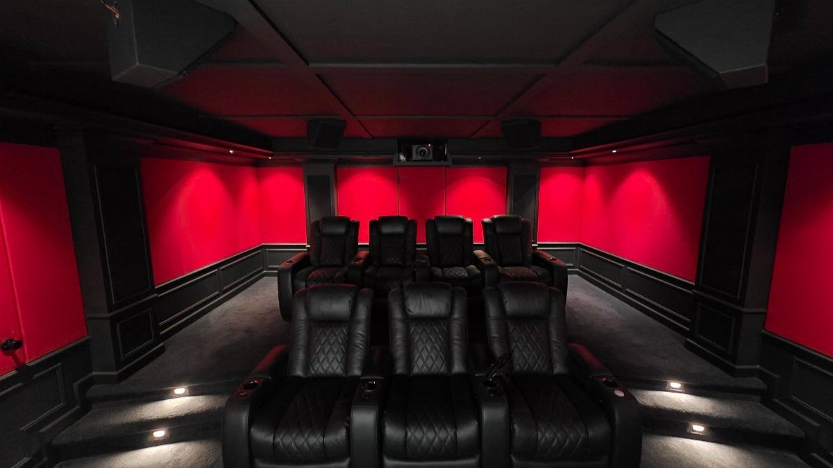 Home cinema room with black leather recliners and red glowing wall panels.