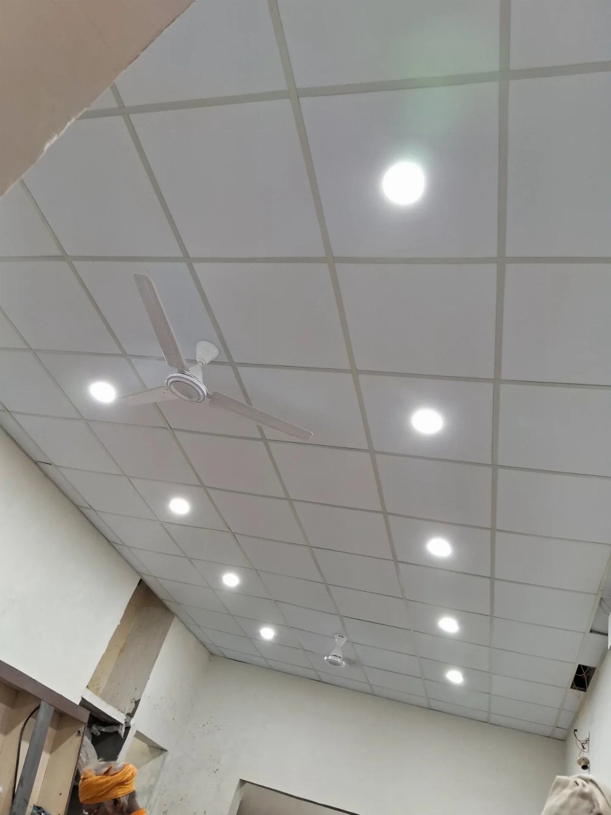 White drop ceiling tiles with recessed lighting and a white ceiling fan.