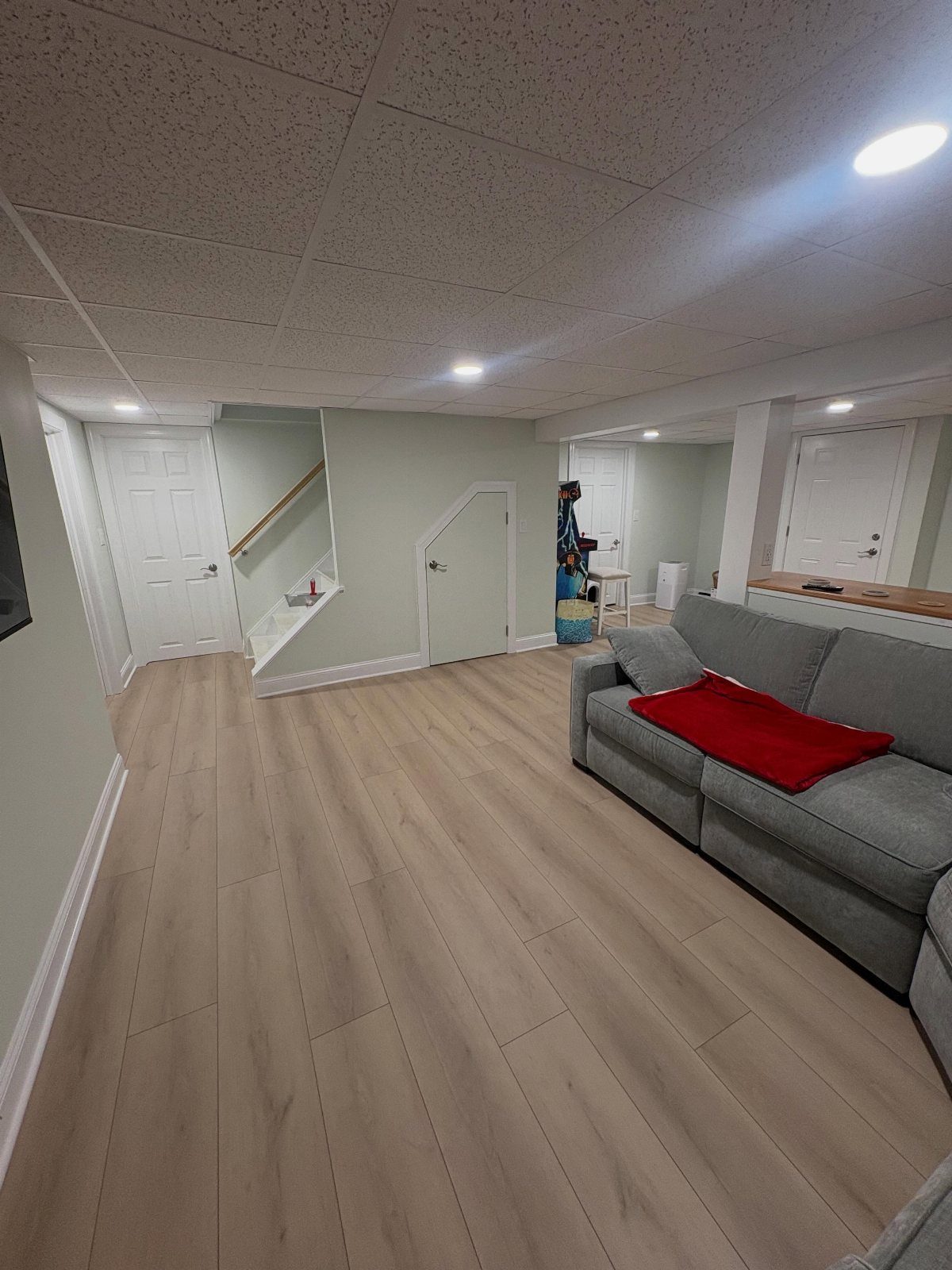 Finished basement interior featuring recessed ceiling lights, plank flooring, and a grey sofa.