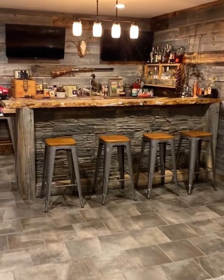 Rustic basement man cave featuring a stone bar with four metal stools and wood paneling.