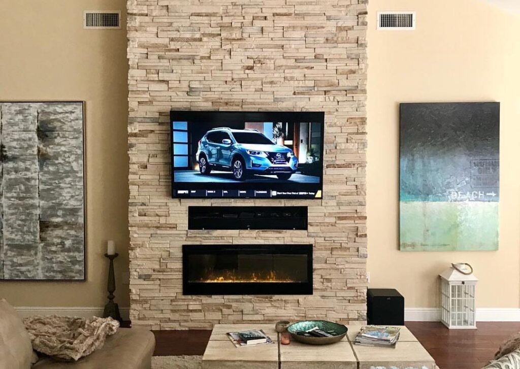 Flat-screen TV mounted above a linear electric fireplace on a stacked stone wall.