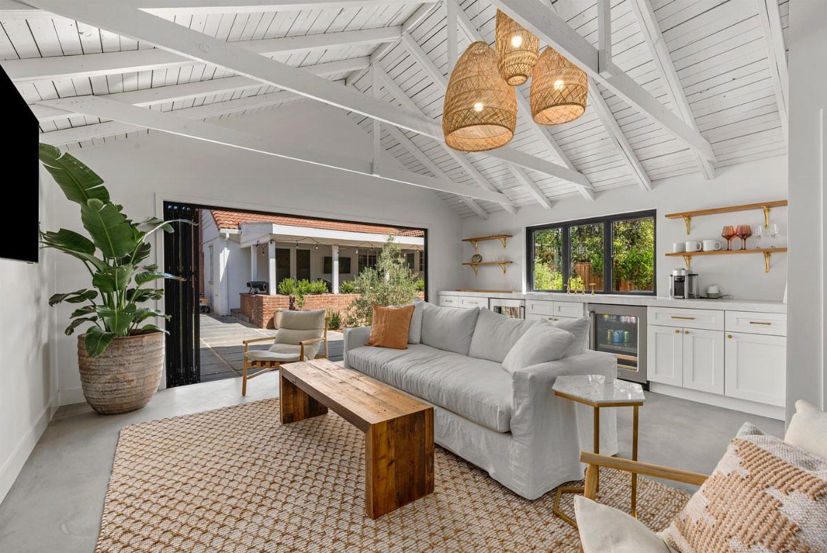 Bright rec room with white vaulted ceilings, grey sofa, and open patio doors.