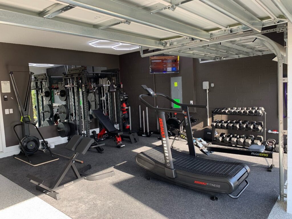 Home garage gym with treadmill, weight bench, and dumbbell rack on rubber flooring