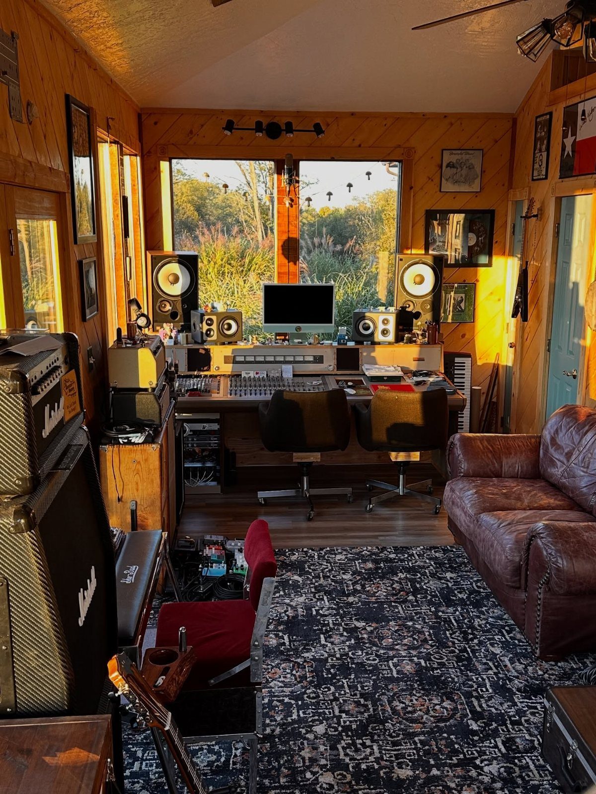 Home music studio with mixing console, studio monitors, and guitar amps in wood-paneled room.