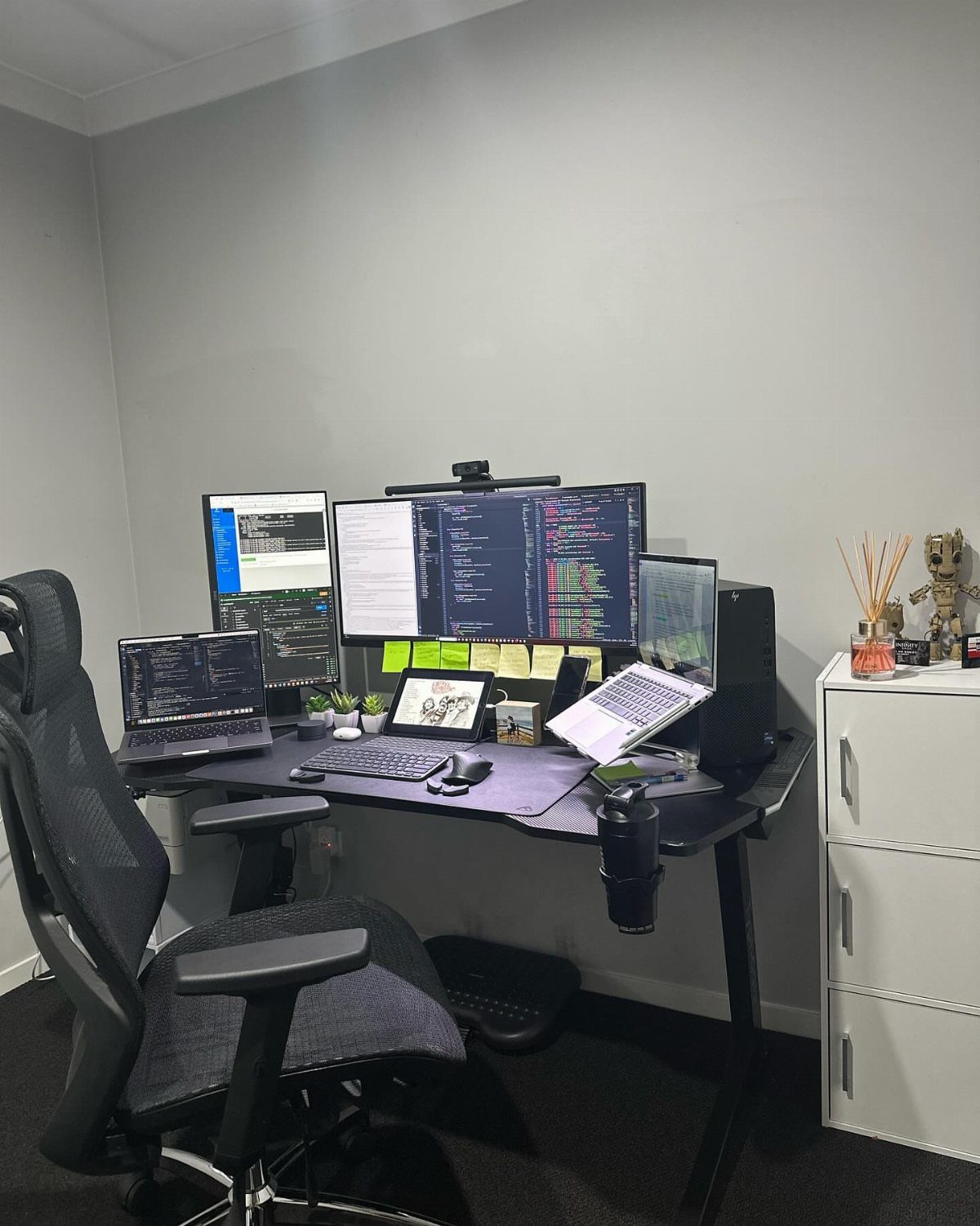 Home office setup with multiple monitors, laptop, and ergonomic chair at a black desk.