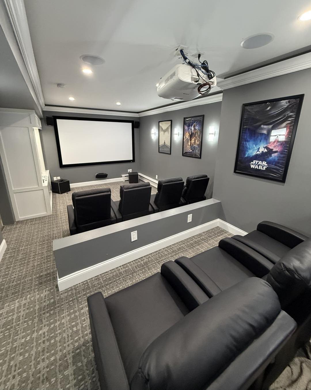 Basement home theater with black leather reclining seats and a large projector screen.