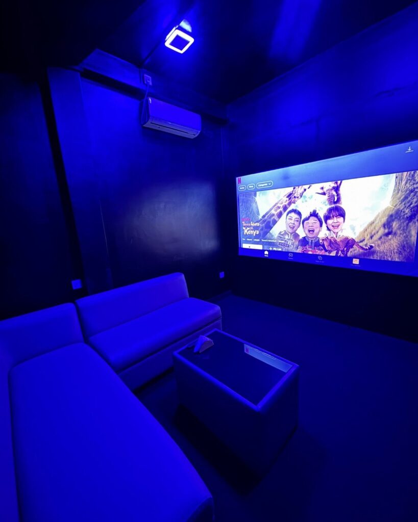 Home theater room with blue lighting, L-shaped sofa, and large movie screen.