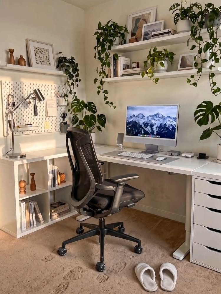 White L-shaped desk setup with a computer, ergonomic chair, and hanging indoor plants.