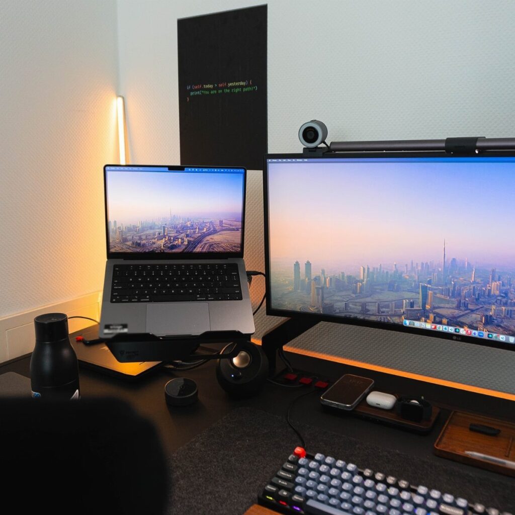 Laptop and widescreen monitor desk setup with mechanical keyboard and city wallpaper