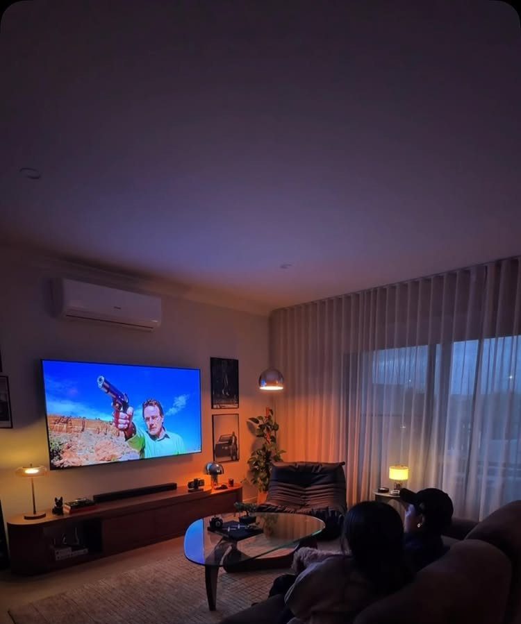 Dimly lit living room with warm ambient lamps and a large movie screen.