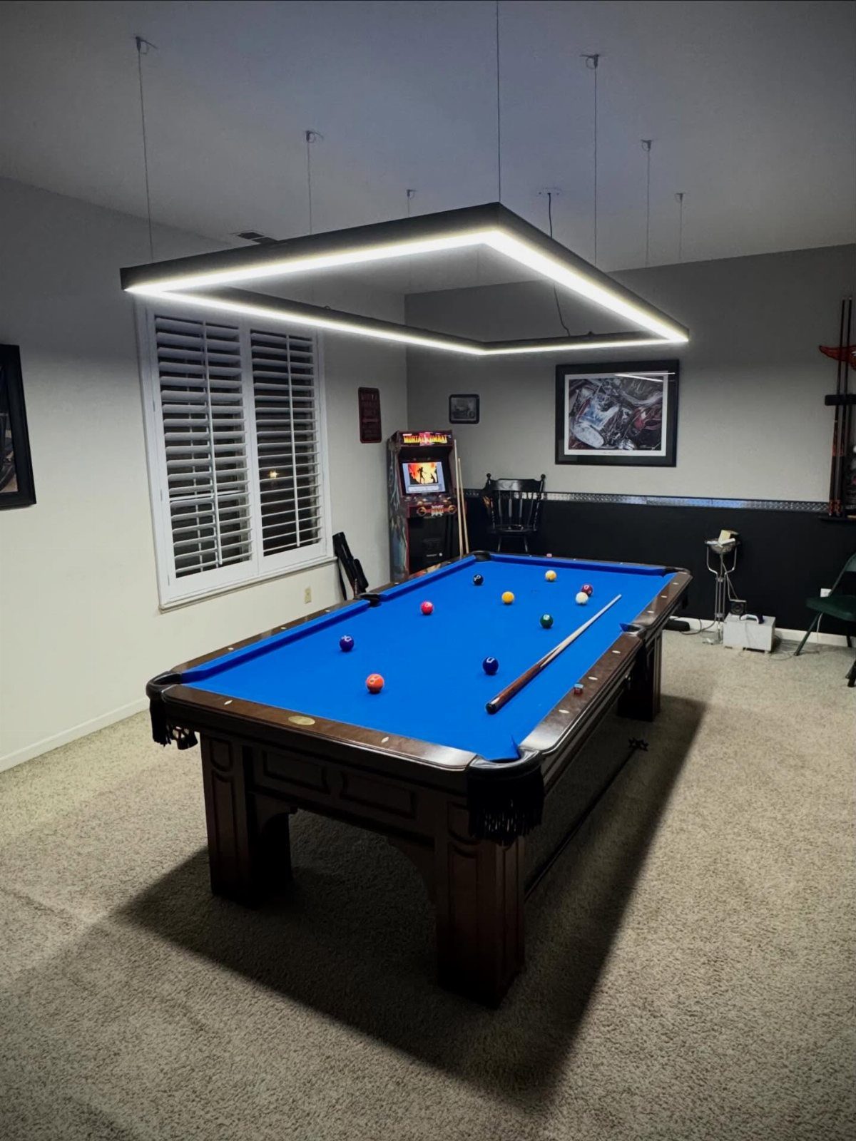 Rectangular LED light fixture hanging over a blue pool table in a game room