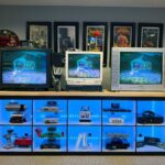 Vintage game consoles displayed in a black shelf with blue LED lighting.