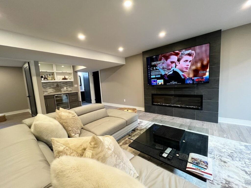 Modern basement living room with a linear fireplace and TV on a grey wall.