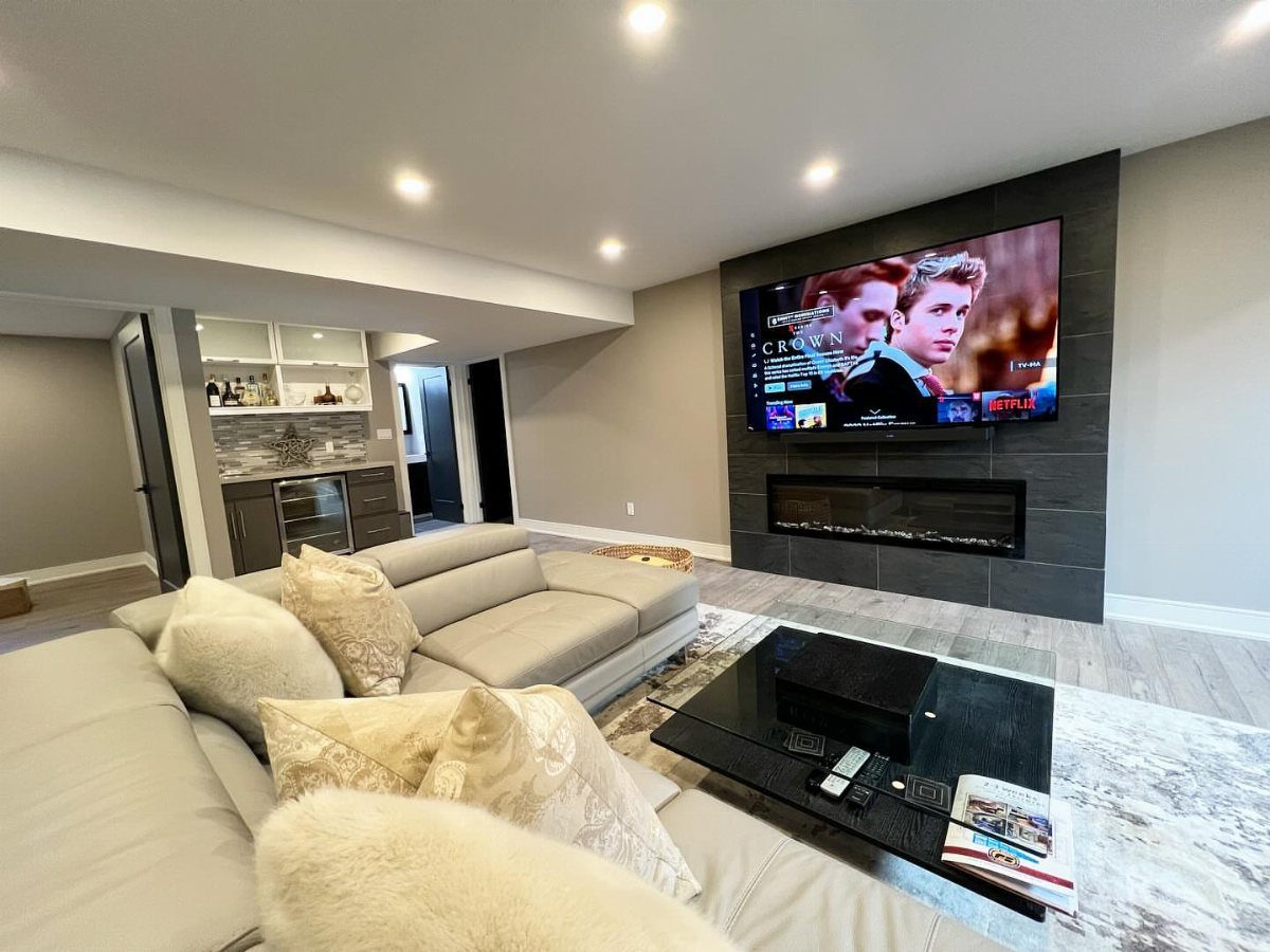 Modern basement living room with a linear fireplace and TV on a grey wall.
