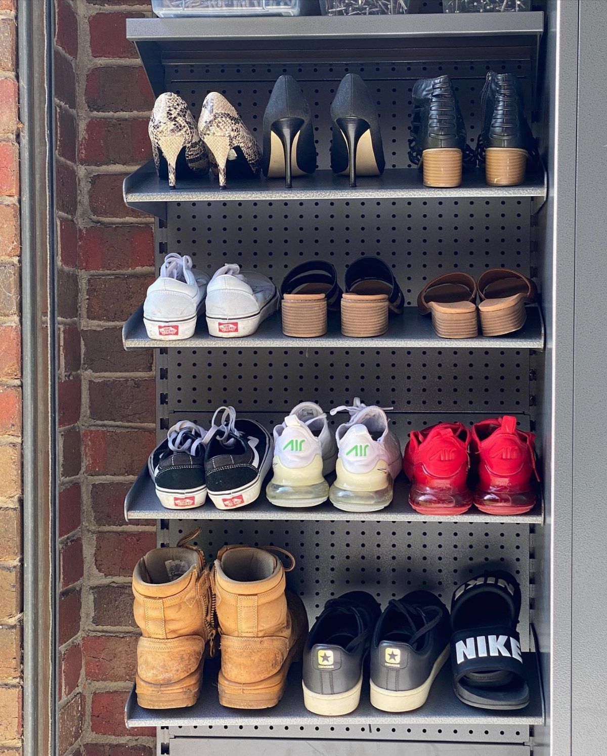 Grey metal shoe rack with various footwear against a red brick wall.