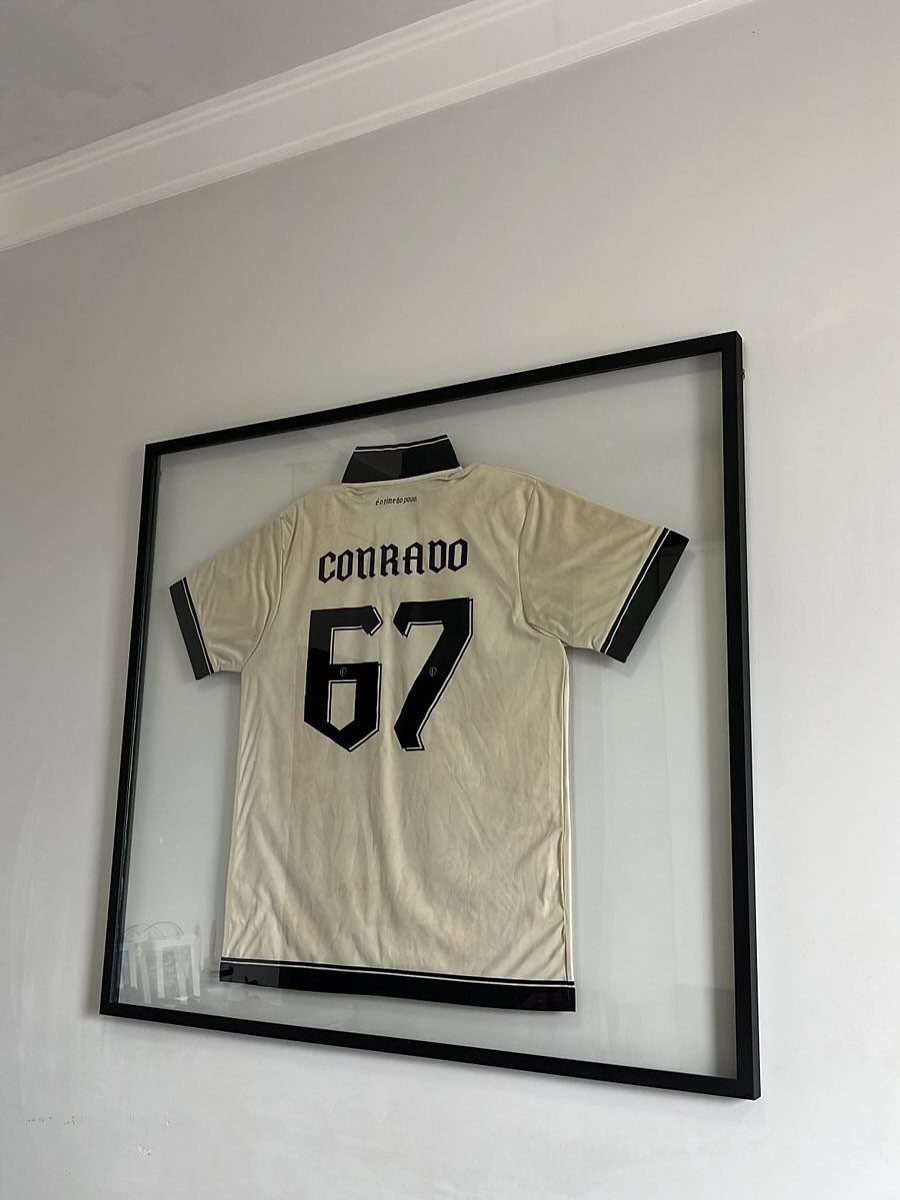 Framed cream sports jersey with black text and number on a grey wall.