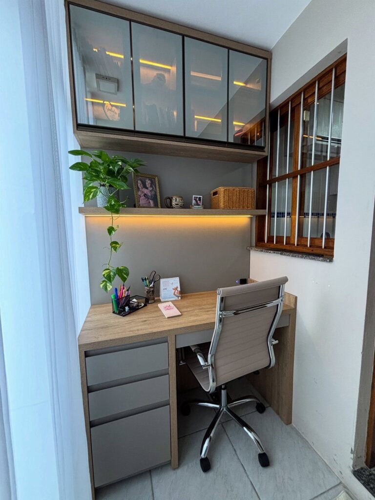 Compact home office with light wood desk, ergonomic chair, and overhead glass cabinets.