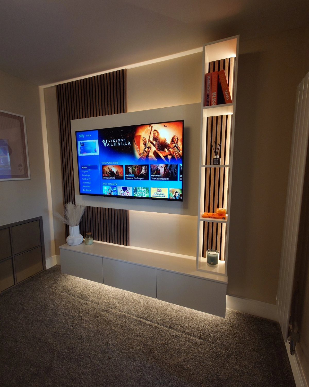 Modern small media room with wall-mounted TV, white floating console, and warm backlighting.