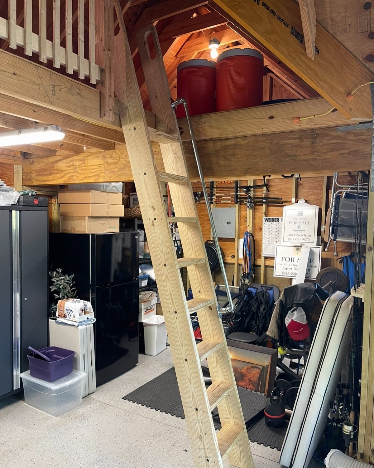 Wooden storage loft in a garage with a ladder and red bins.