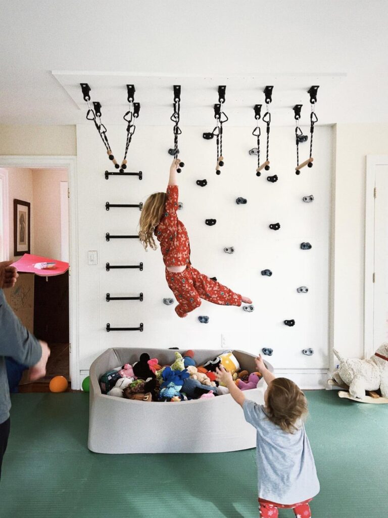 Child climbing a wall with holds next to a bin of plush toys.